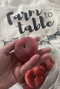 A person holding peaches in a bag with the logo Farm to Table.